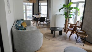 Ein modernes Wohnzimmer mit einem grauen Sofa, einem runden Couchtisch und einem Essbereich mit einem Holztisch und Stühlen.