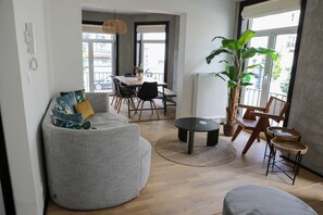 Ein modernes Wohnzimmer mit einem grauen Sofa, einem runden Couchtisch und einem Essbereich mit einem Holztisch und Stühlen.