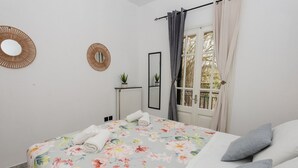A bedroom with a floral bedspread, a radiator, a mirror, and a window with curtains. - Philomena Apartment by Ionian Luxury (Kerkira)