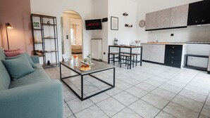 A modern living room with a sofa, coffee table, and a kitchen area with cabinets and a refrigerator. - Philomena Apartment by Ionian Luxury (Kerkira)