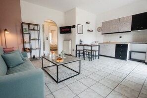 A modern living room with a sofa, coffee table, and a kitchen area with cabinets and a refrigerator. - Philomena Apartment by Ionian Luxury (Kerkira)
