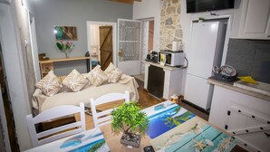 A cozy room with a bed, a dining table with a plant, a TV, a microwave, and a refrigerator. - Archontissa House - Sea View (Mesongi)