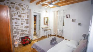 Una camera da letto con un letto, un soffitto in legno, un muro in pietra, un bagno con un lavandino e uno specchio.