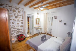 A bedroom with a bed, a wooden ceiling, a stone wall, a bathroom with a sink, and a mirror. - Archontissa House - Sea View (Mesongi)