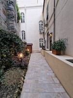 A narrow stone pathway flanked by buildings with arched windows and a small wooden structure.