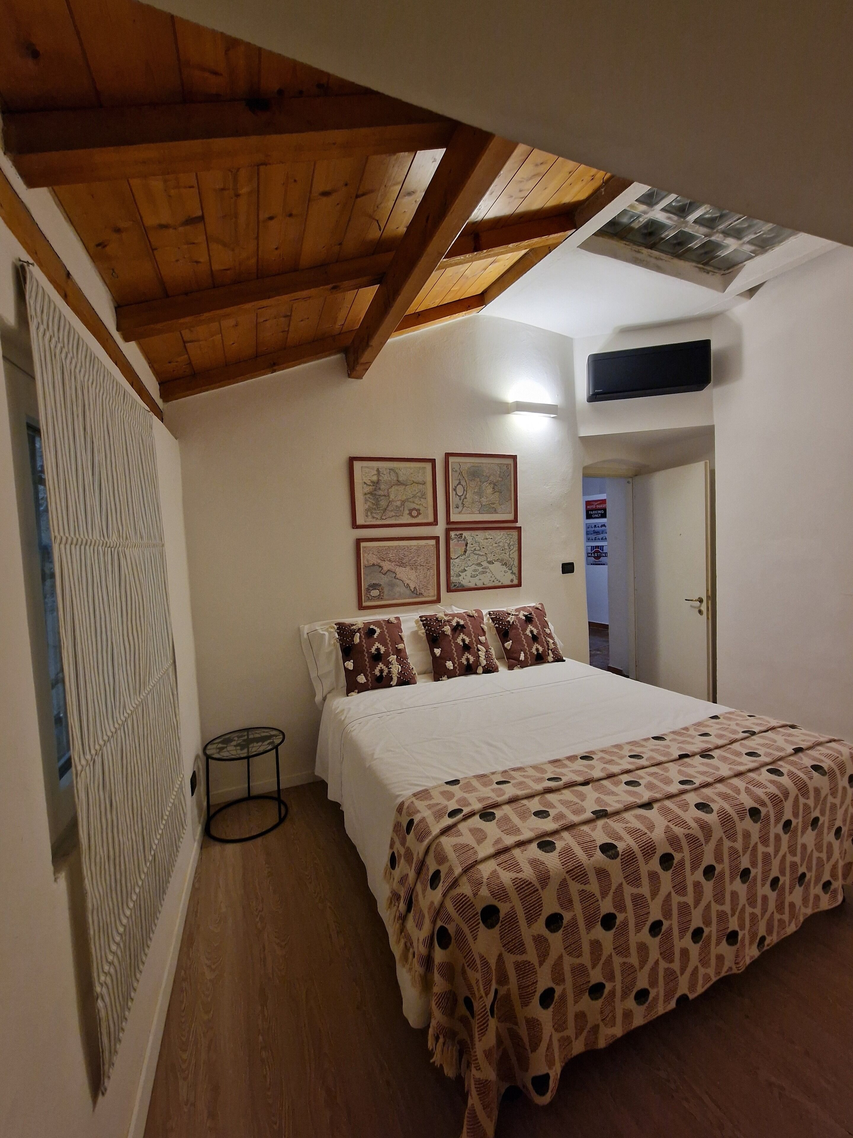 Een slaapkamer met een houten plafond, een bed met beddengoed met een patroon, een klein rond tafeltje en lijstwerken aan de muur.
