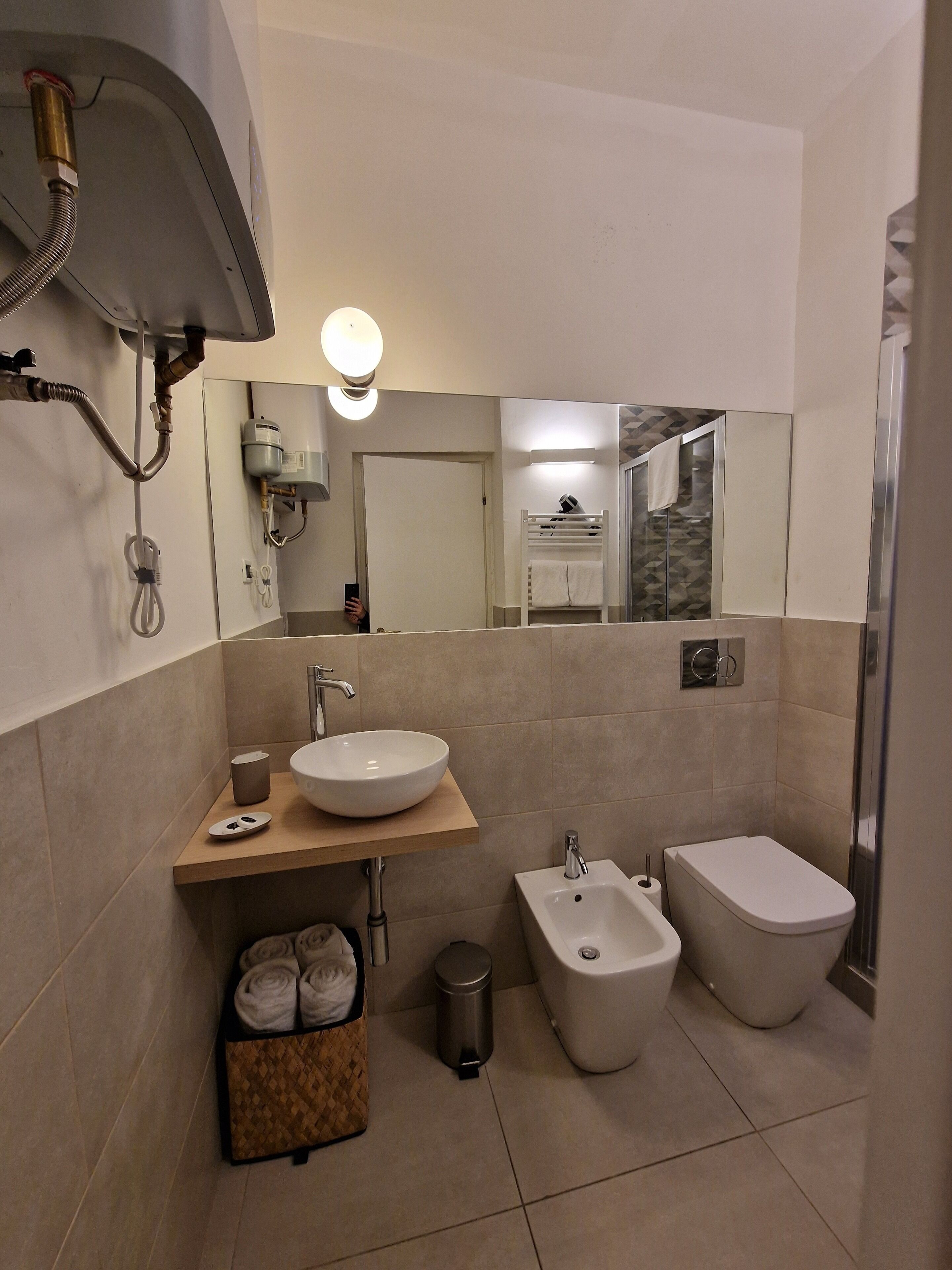 Um banheiro moderno com uma pia grande, bidê e vaso sanitário. Há um espelho, porta-toalhas e uma lixeira.