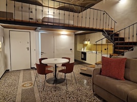 A compact living space with a dining area, a sofa, a staircase, and a kitchen.