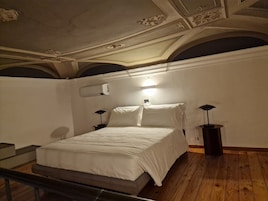 Quarto com cama, duas mesas de cabeceira, ar condicionado e uma luminária.