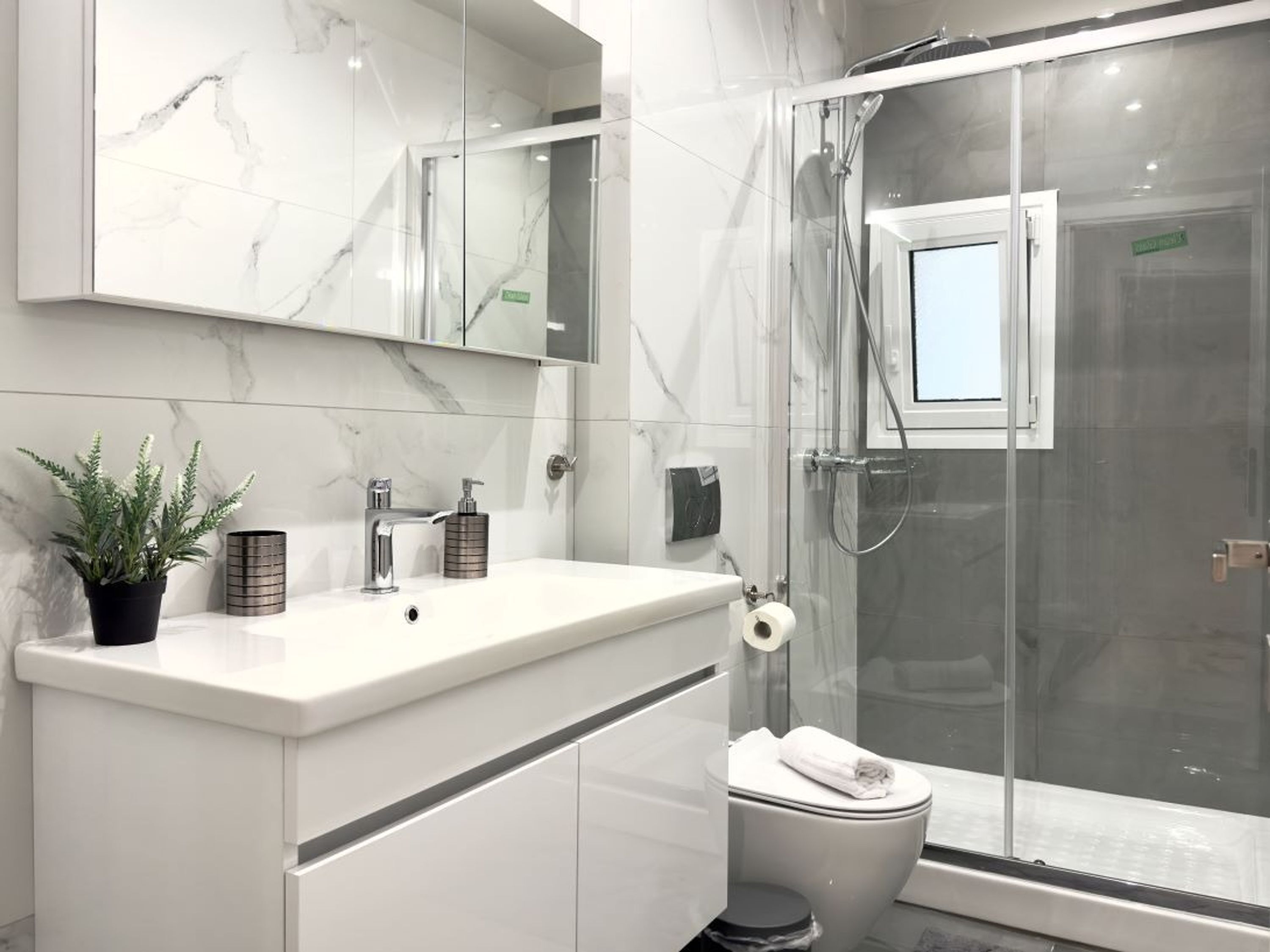 A modern bathroom with a marble vanity, a glass shower enclosure, and a toilet.