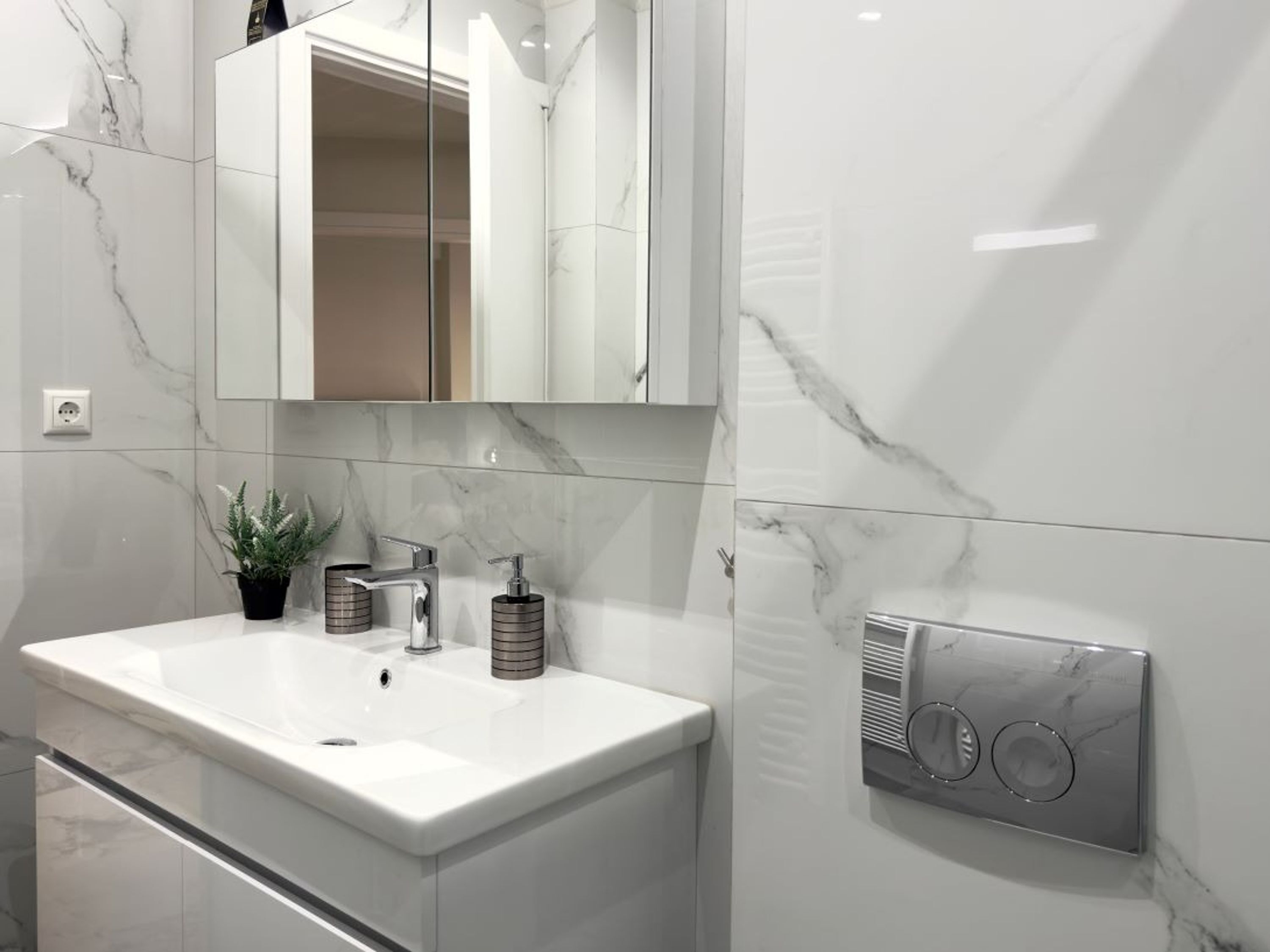 A modern bathroom with a white marble sink, a mirror above it, and a wall-mounted ventilation unit.