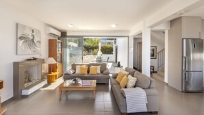 A modern living room with a sofa, coffee table, and fireplace. There is a large window providing a view of the outdoors. - Lenias Sea View in Neo Chorio (Neo Chorio)