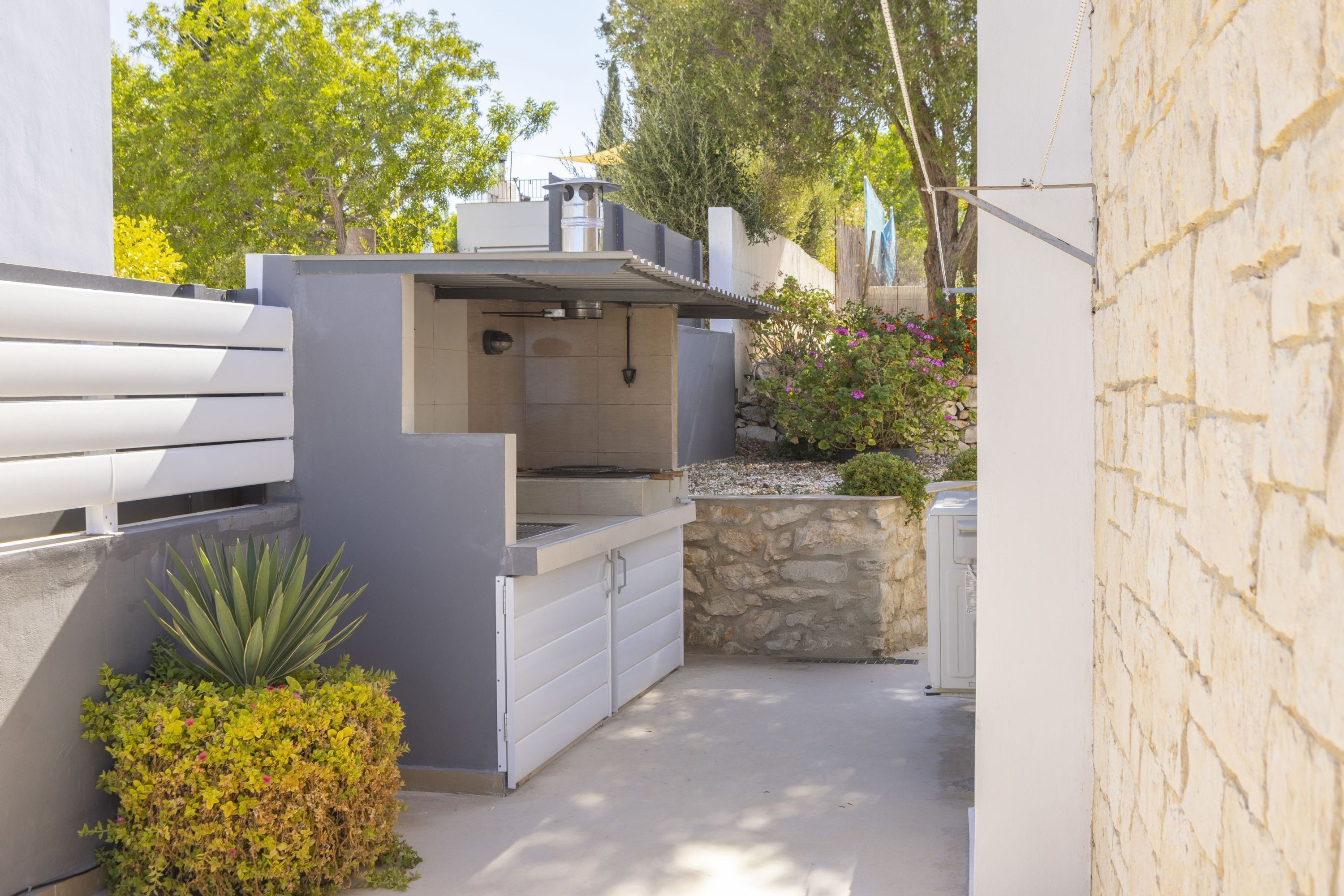 Un área de cocina exterior moderna con una parrilla empotrada, pared de piedra y plantas en macetas.