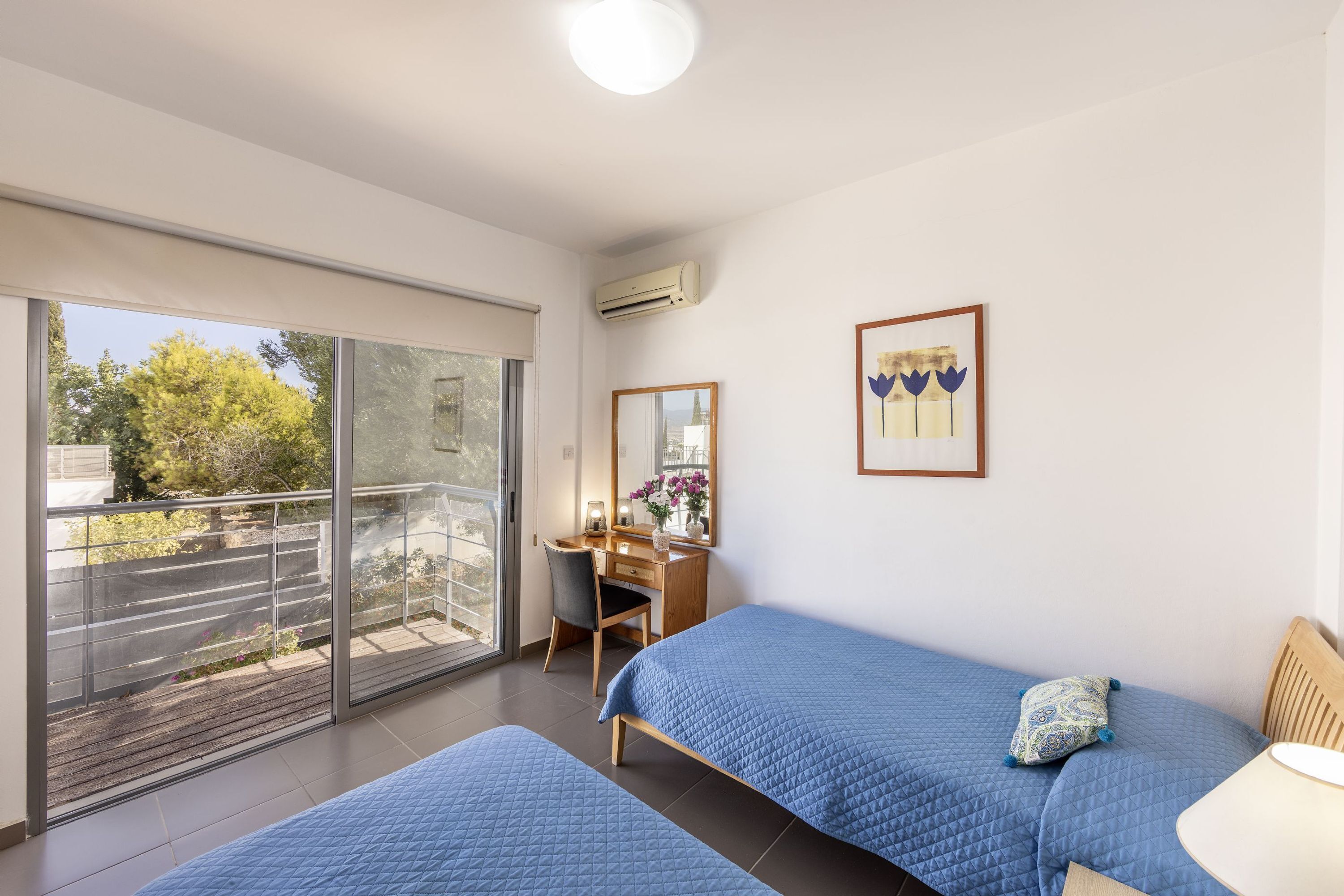 A bedroom with two beds, a desk, and a large sliding glass door to a balcony.