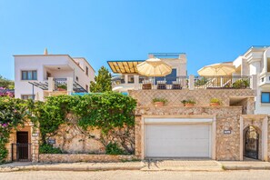 A residential building with a stone facade, a garage, and outdoor seating with umbrellas. - Villa Vanilla in Kalkan (Kalkan)
