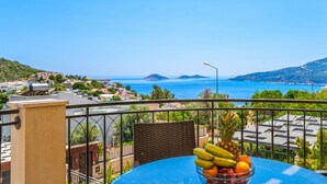 Een balkon met een tafel en een schaal fruit, met uitzicht op een kustplaats en de zee.
