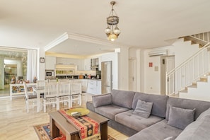 A spacious living area with a grey sofa, a wooden coffee table, and a dining table with chairs. A kitchen is visible in the background, and a staircase leads to another level. - Villa Vanilla in Kalkan (Kalkan)