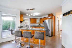 A modern kitchen with wooden cabinets, a stainless steel refrigerator, and a bar area with stools.