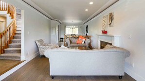 Een ruime woonkamer met een grote grijze bank, een gestreept fauteuil en een houten trap naar een hoger niveau.