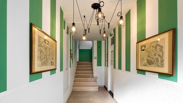Ein Korridor mit grün-weißen Wänden, gerahmten Bildern, einer Treppe und hängenden Leuchten.