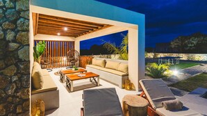 An outdoor patio with a stone wall, wooden furniture, and a view of the night sky. - Aiolia Villa in Rhodes (Rhodes)