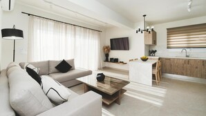A modern living room with a sofa, coffee table, and a dining area with a kitchen in the background. - Aiolia Villa in Rhodes (Rhodes)