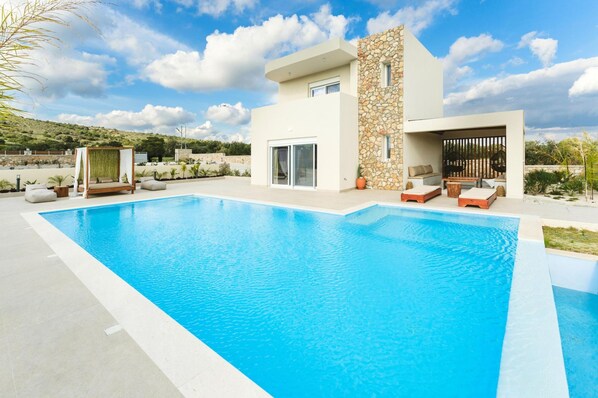 A modern house with a swimming pool, outdoor seating, and a stone facade. - Aiolia Villa in Rhodes (Rhodes)
