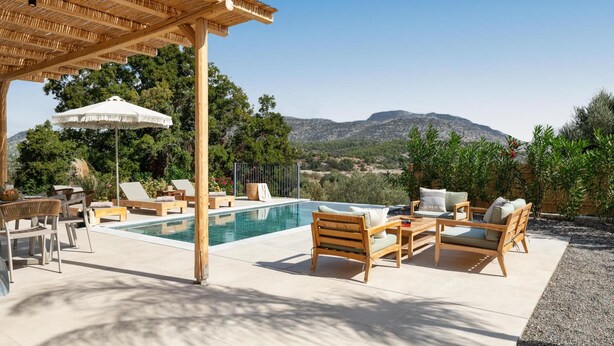 Zona junto a la piscina con mobiliario de madera, una pérgola y vistas a las montañas.