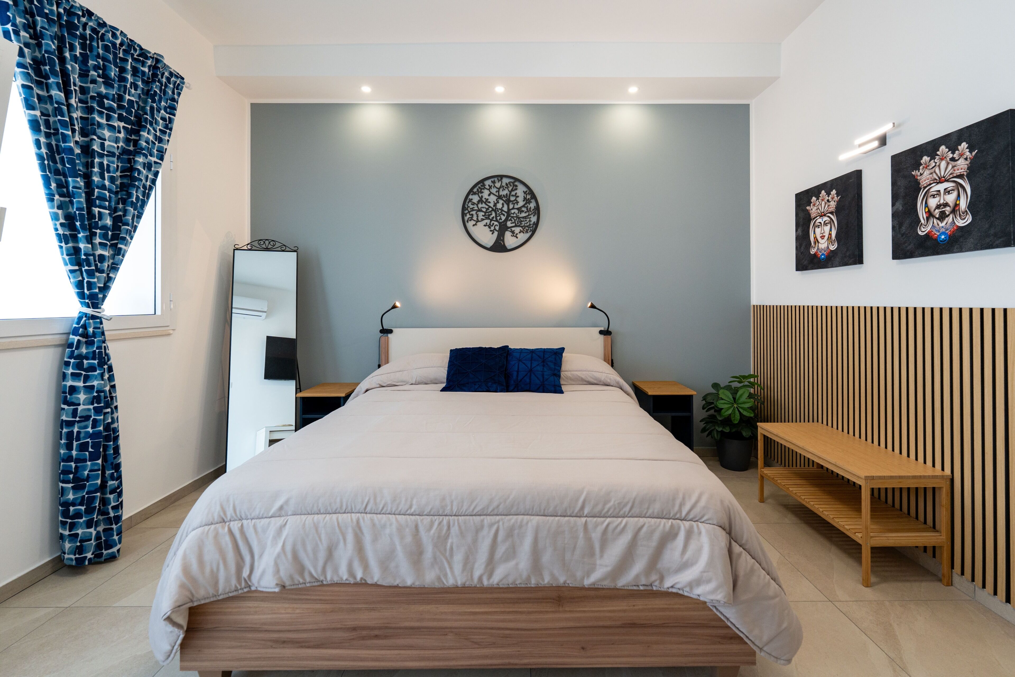 A modern bedroom with a bed, bedside tables, a mirror, and artwork on the wall.