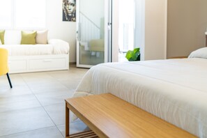 Une chambre à coucher moderne avec un grand lit, un banc en bois, un canapé blanc et une plante verte.