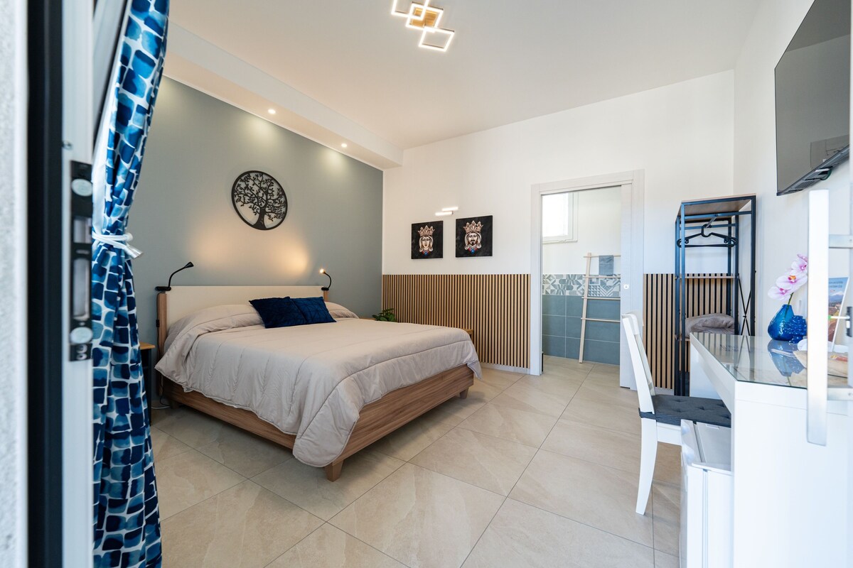 A modern bedroom with a bed, a desk, and a TV.
