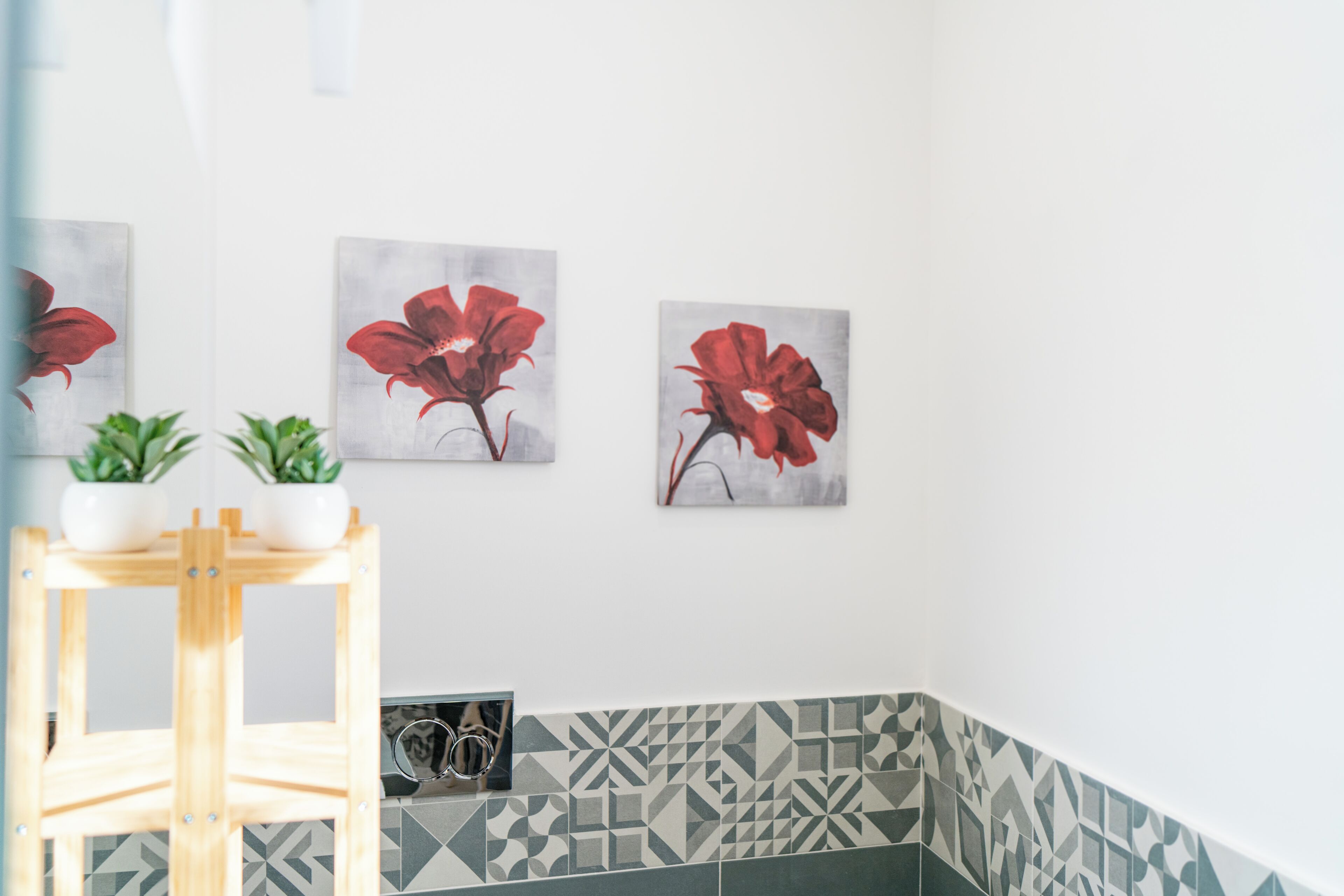 Una esquina de una habitación con una silla de madera, dos plantas en macetas y tres cuadros colgados en la pared con flores rojas.