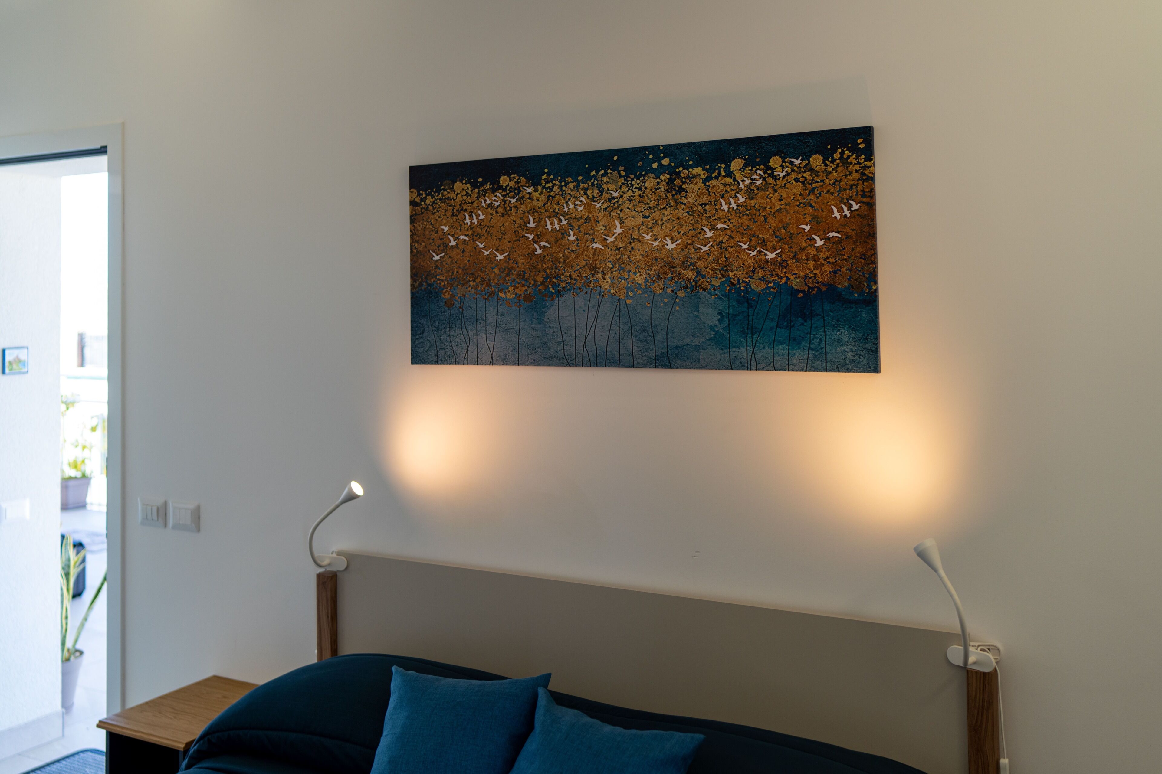 Ett rum med en säng, en vägglampa och en tavla.