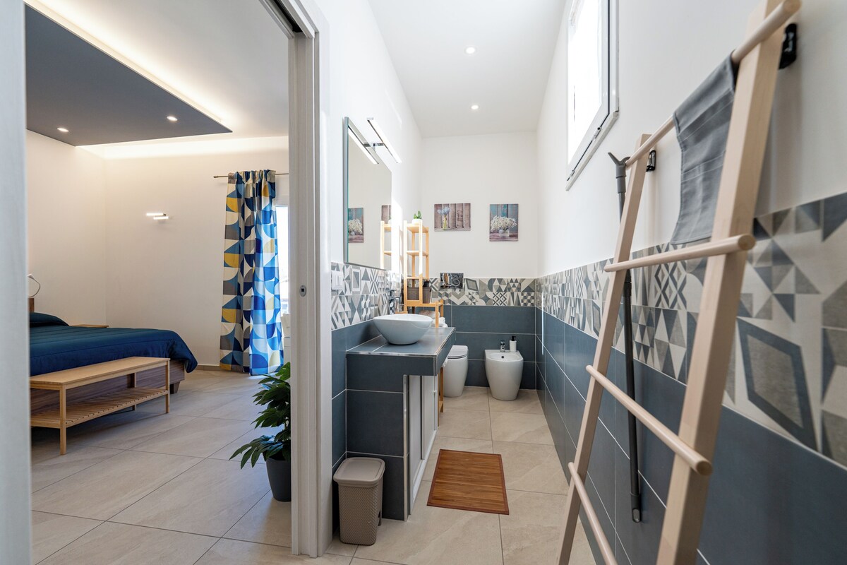 A modern bathroom with a bathtub, toilet, and sink. There is a shower curtain and a potted plant.