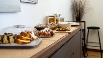 Un banco buffet con diversi cibi, tra cui pasticcini e pane, e un angolo per il caffè.