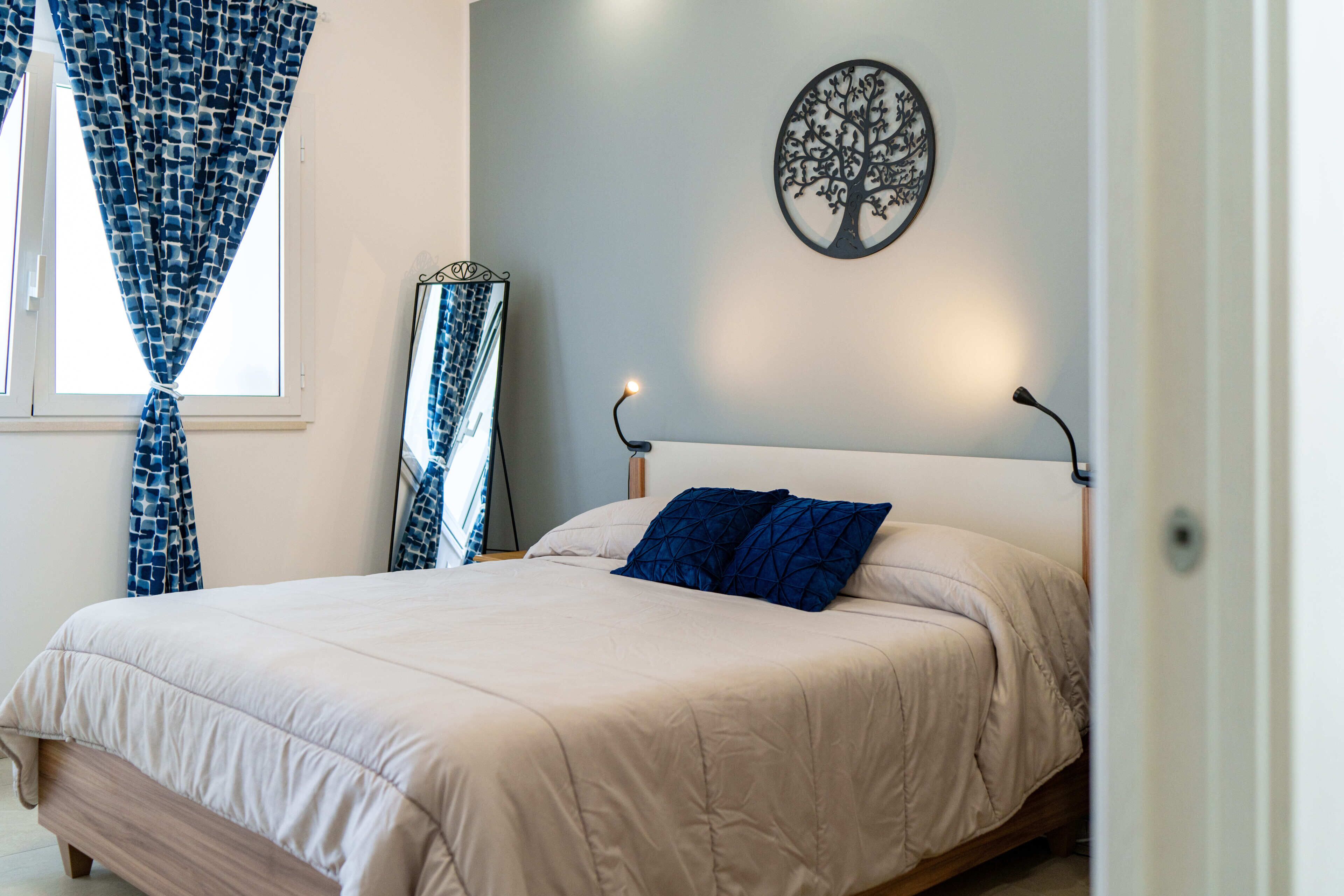Un dormitorio con cama, un adorno de árbol en la pared y una ventana con cortinas.