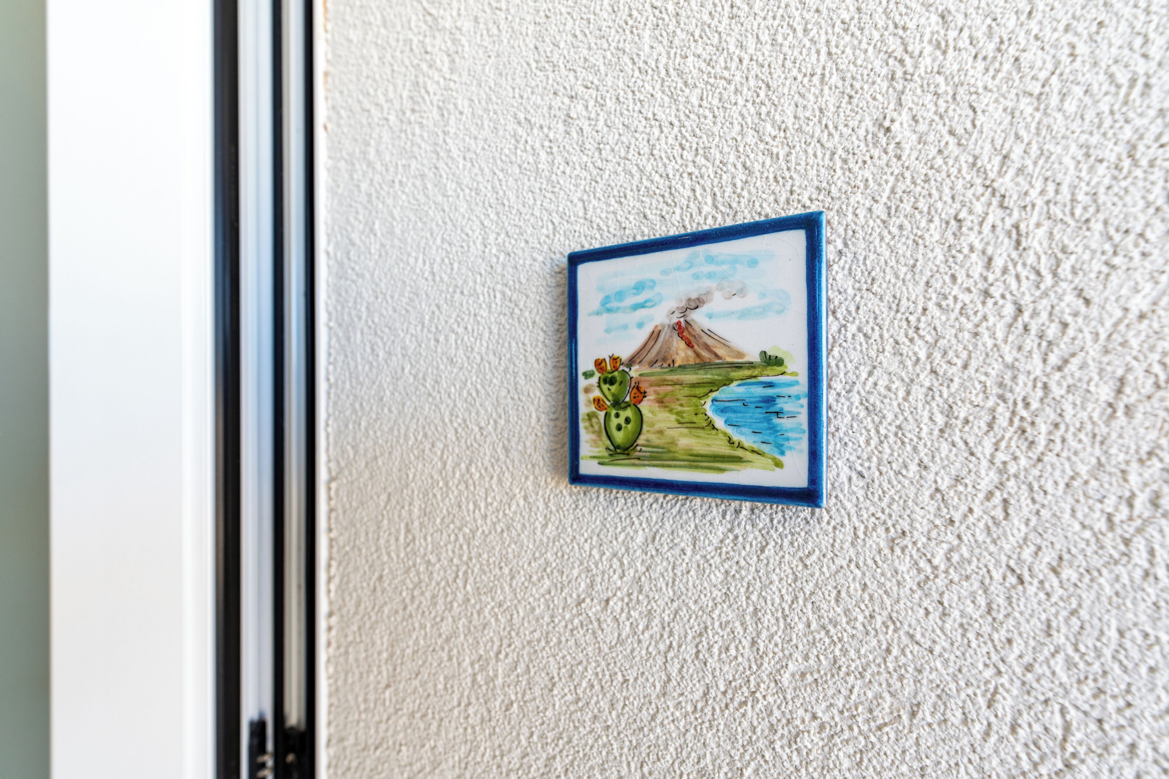 A framed picture of a volcano and cactus on a textured wall.