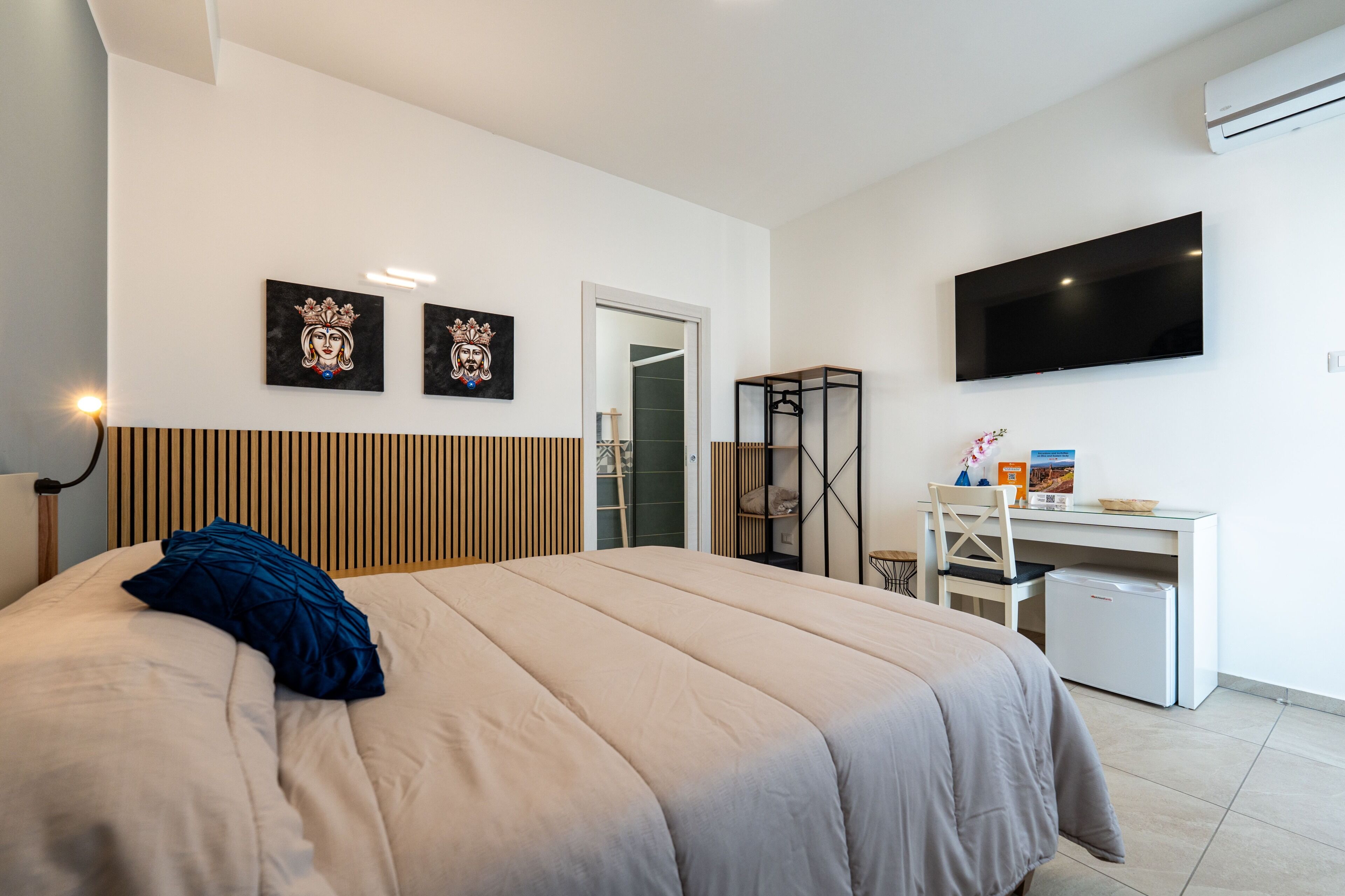 A modern hotel room with a large bed, a desk, a flat-screen TV, and artwork on the wall.