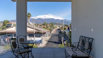 Un balcón con dos sillas y una mesa, con vista a una calle con casas y una montaña nevada en la distancia.