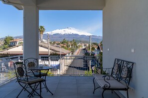 Ein Balkon mit zwei Stühlen und einem Tisch, mit Blick auf eine Straße mit Häusern und einem schneebedeckten Berg im Hintergrund.
