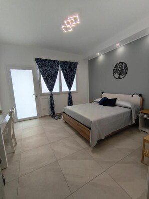 A bedroom with a bed, a desk, and a chair. There is a window with curtains and a wall decoration.