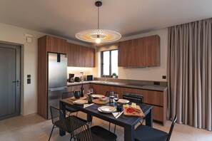 A modern kitchen with wooden cabinets, a built-in refrigerator, and a dining area with a table set for four. - Massari Hills- Villa Finis Terrae 2 (Rhodes)