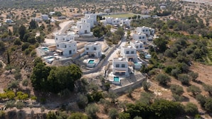 A modern residential area with white buildings, green swimming pools, and a hilly landscape in the background. - Massari Hills- Villa Finis Terrae 2 (Rhodes)