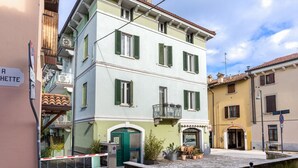 Un edificio a più piani con una porta verde, un balcone e un cartello che indica una località vicina.
