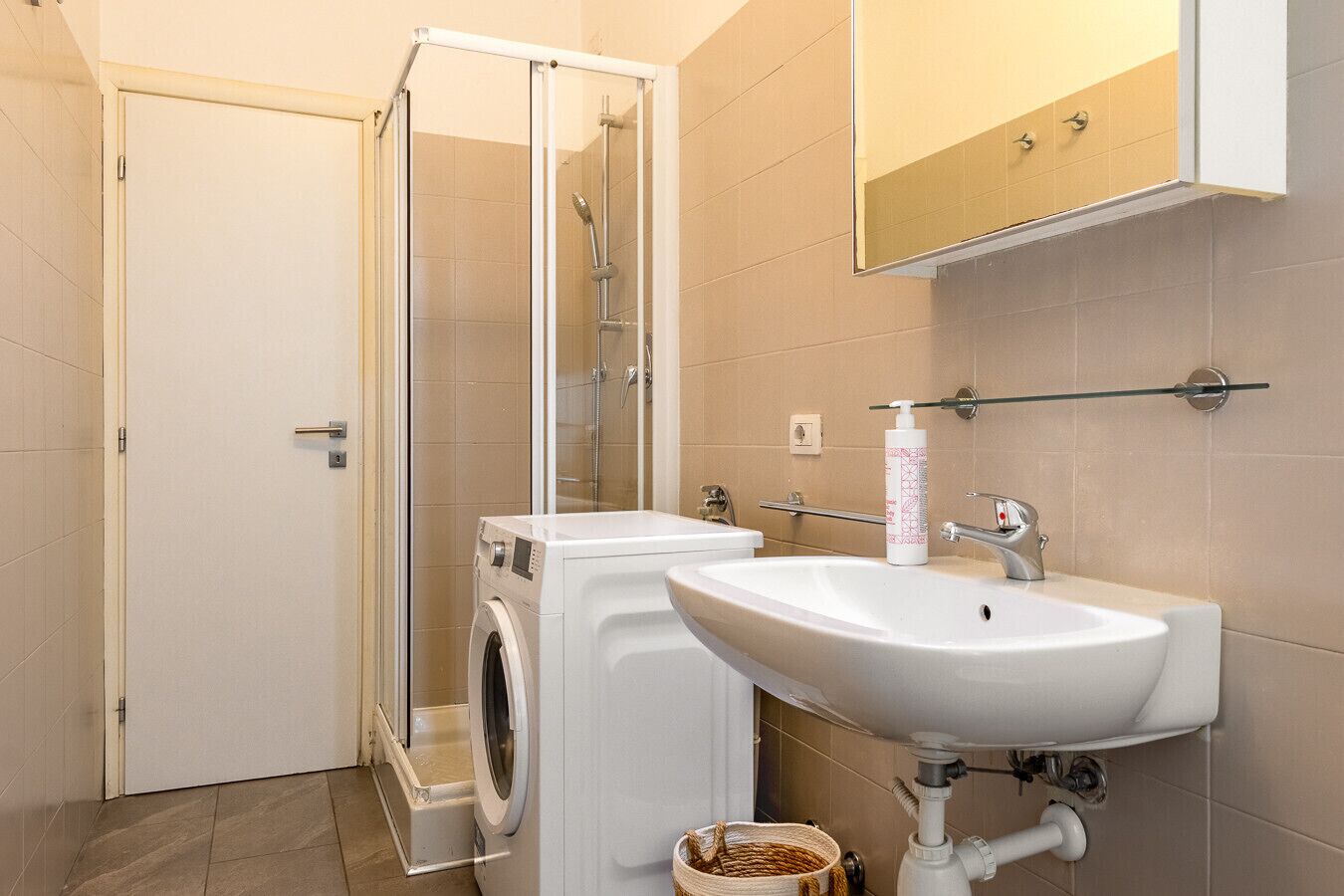 A bathroom with a glass-enclosed shower, a washing machine, a sink, and a towel rack.