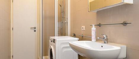 A bathroom with a glass-enclosed shower, a washing machine, a sink, and a towel rack.