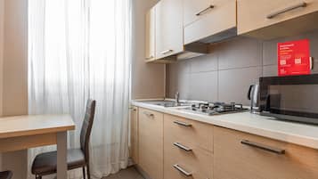 A compact kitchen with a microwave, toaster, and kettle. There is a dining table with a chair, and a red welcome sign on the wall.