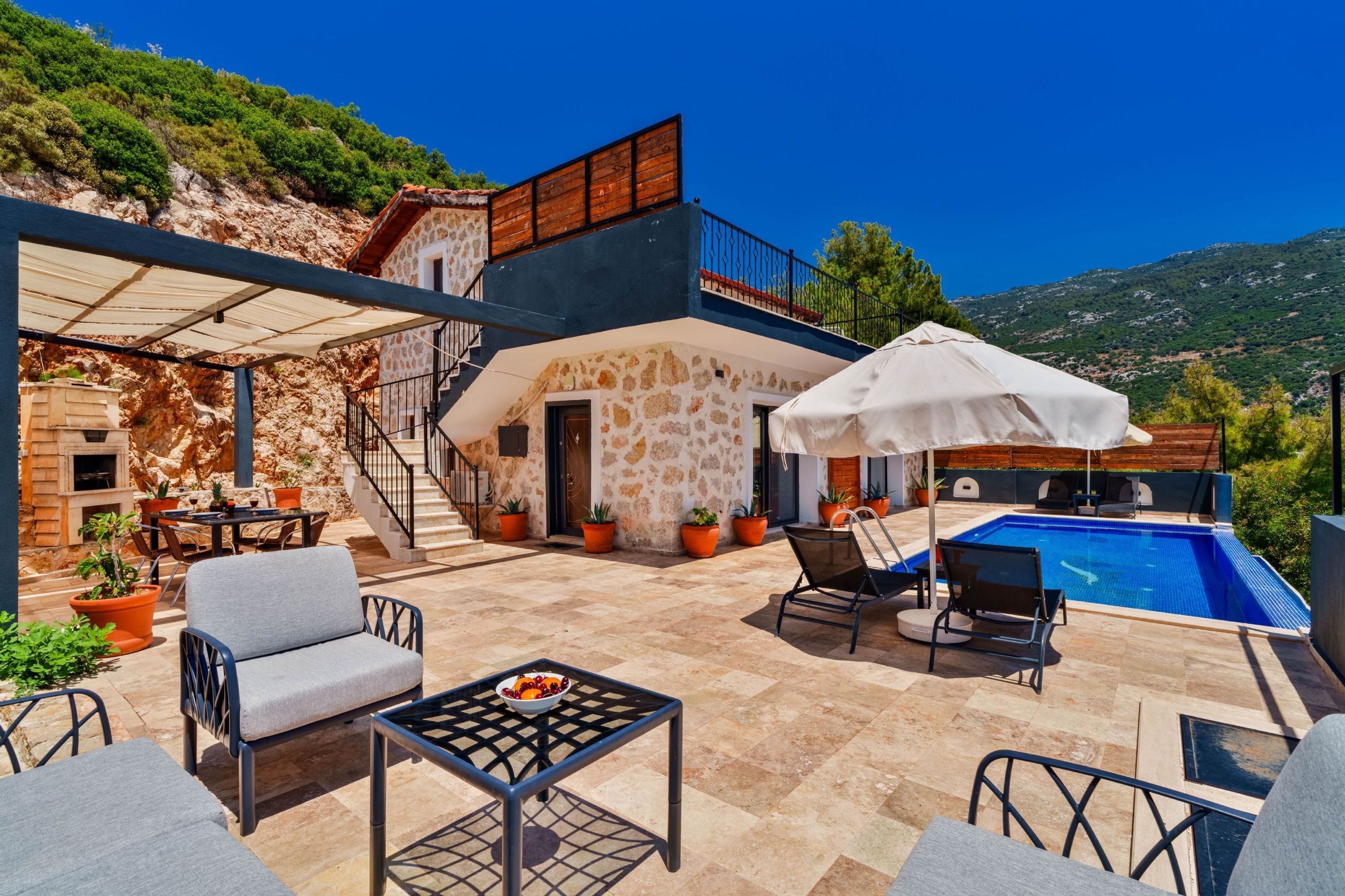 Una villa con fachada de piedra, piscina, zona de estar al aire libre y una escalera que lleva a un balcón.