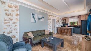 En moderne stue med sofa, sofabord og et køkkenområde med bar og køleskab.