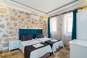 A hotel room with two beds, a white nightstand, a white desk, and a stone-patterned wall. - Villa Safi in İslamlar Köyü (İslamlar Köyü)